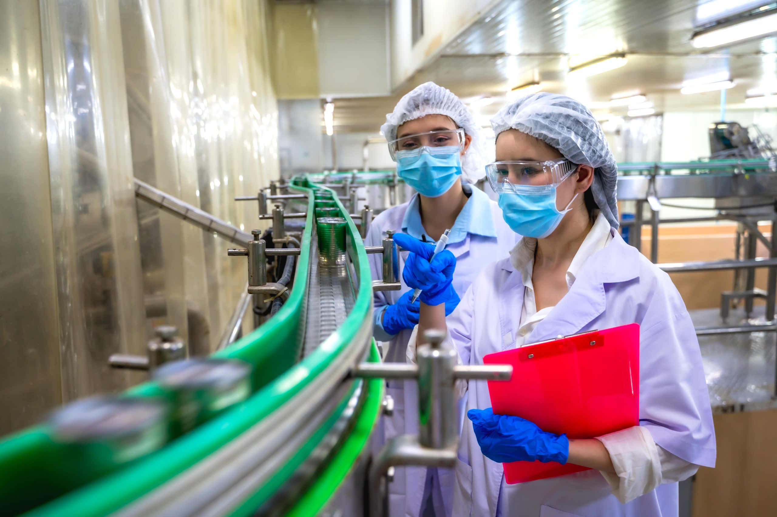 Women food safety inspectors in hairnets and gowns inspecting canning process at a modern manufacturing plant